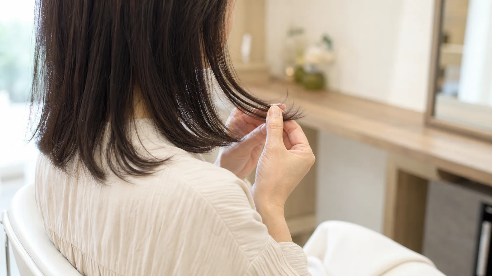 毛先を手に取って髪の質感を確かめている女性